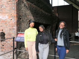Three smiling teenagers in front a the brick walls of a historic furnace