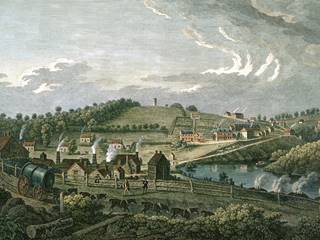 coloured print showing Coalbroodklae in 1758. The landscape has a number of green fields in the fore ground and distance, with a lake in the middle distance. There are lots of buildings - houses as well as larger industrial buildings - scattered across the image, all giving off smoke. In the foreground a team of horses pull a metal cylinder - a boiler for a new steam engine. They are about to pass four smoking stacks of wood, used to make charcoal. 