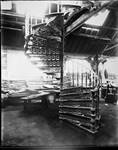 Glass plate negative of a cast-iron spiral staircase, most likely taken inside the fitting workshop, c. 1900. [1986.14020]