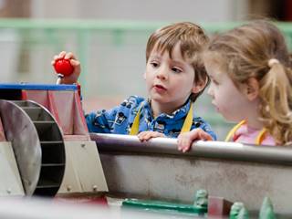 A young boy and girl look inquisitively as they play with an interactive water wheel, part of the power valley exhibit at Enginuity.