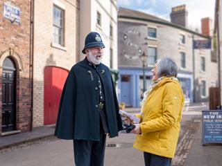 A man dressed as a Victorian police officer engages with a lady in the streets of Blists Hill Victorian Town, both people are smiling and having a great time.