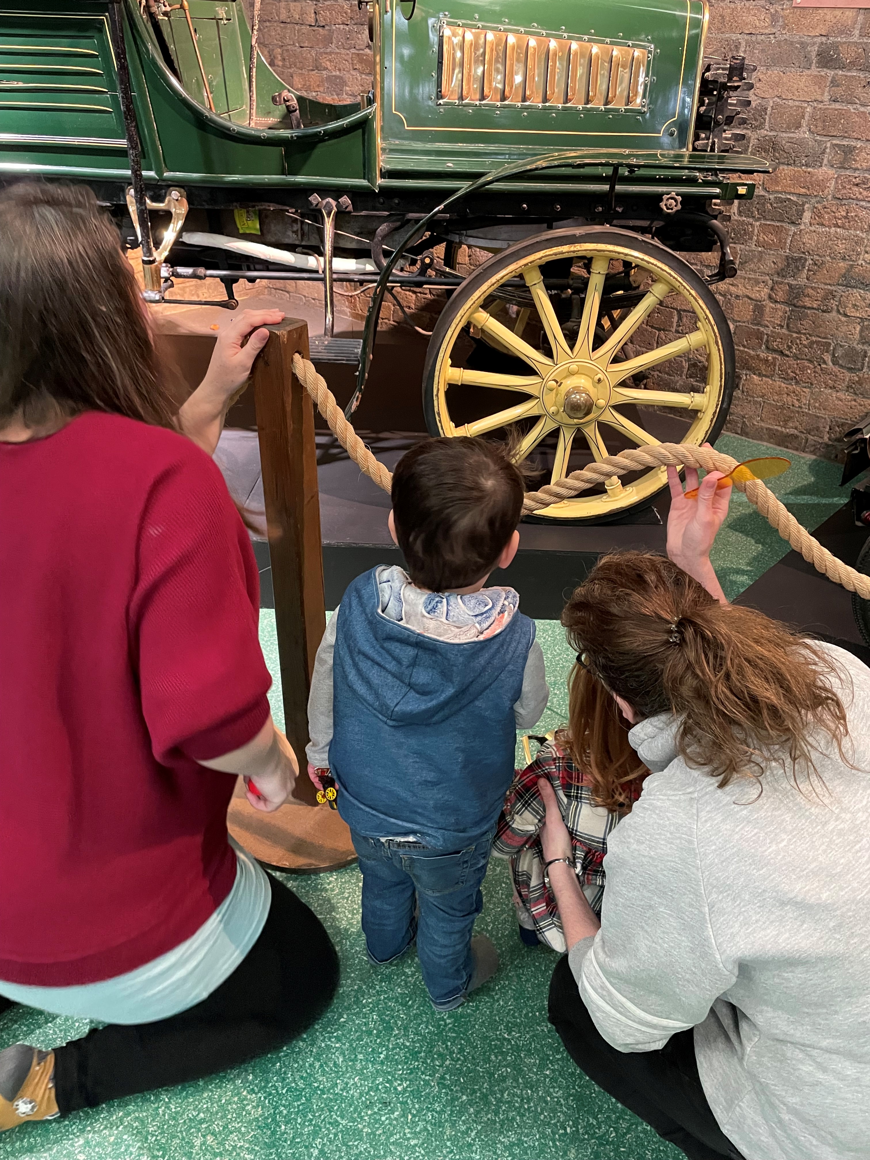 A family are looking at an old-fashioned car inside Enginuity.